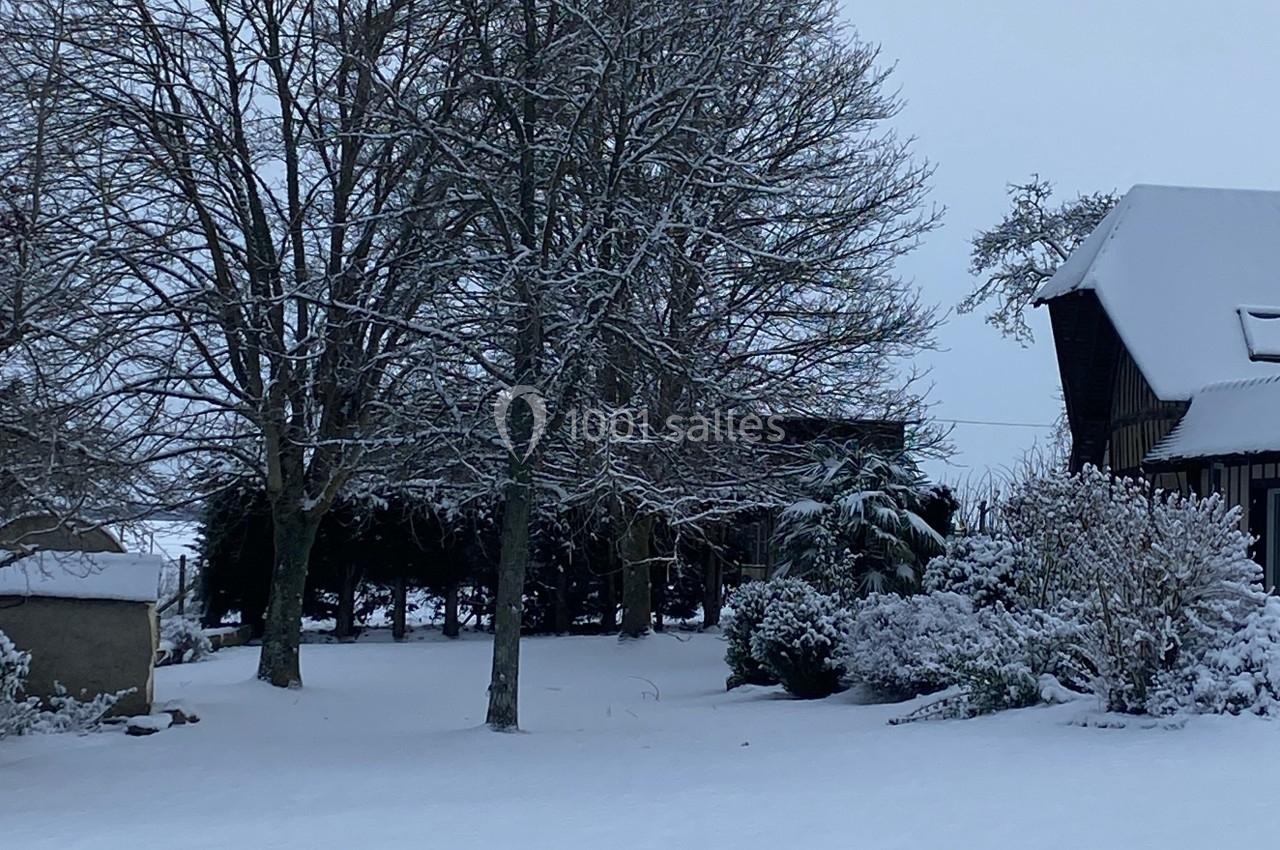 Paysage hivernal avec arbres dénudés et toits enneigés dans un jardin recouvert de neige.