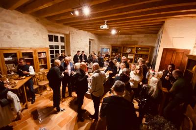 Grande salle vide avec un sol en pierre, plafond en bois avec poutres apparentes et lustres suspendus, décorée de plantes.