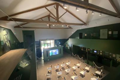 Grande salle vide avec un sol en pierre, plafond en bois avec poutres apparentes et lustres suspendus, décorée de plantes.