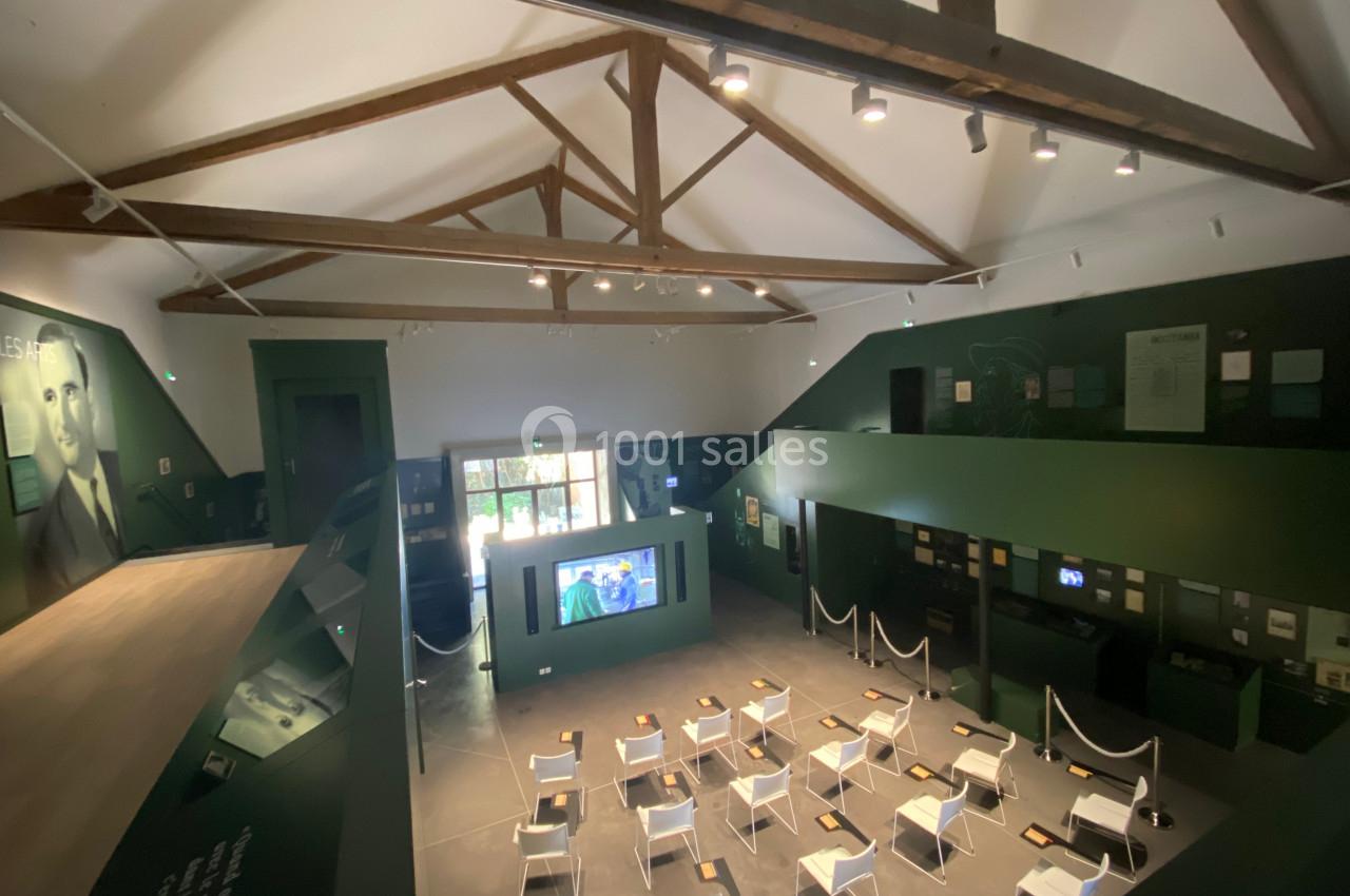 Salle d'exposition avec des chaises alignées, des panneaux informatifs sur les murs et un écran au fond.