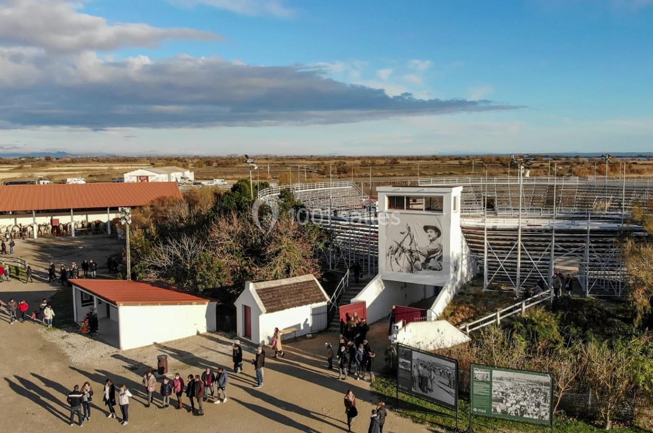 Vue aérienne d'une arène en plein air entourée de bâtiments, avec des visiteurs se promenant dans un espace dégagé.