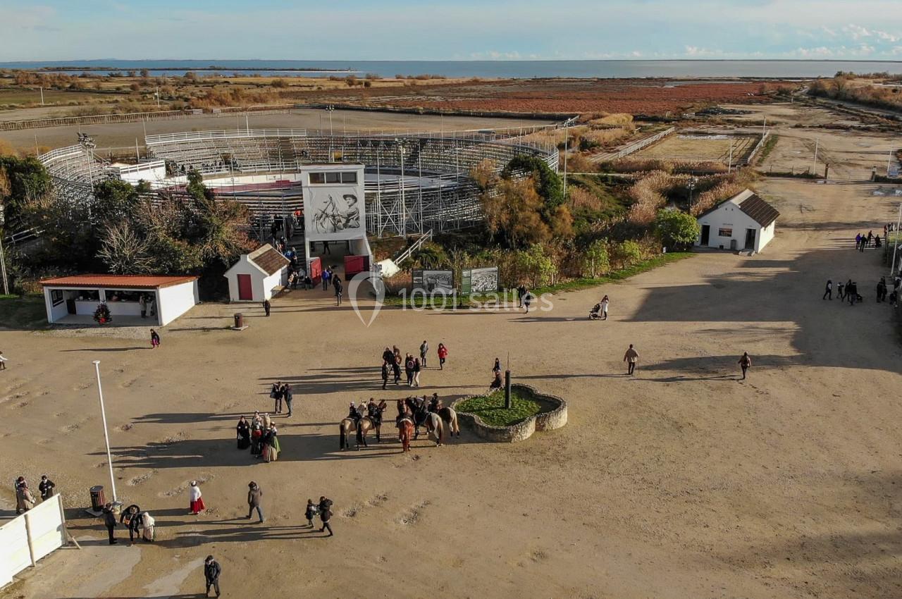Vue aérienne d'une arène entourée de bâtiments et de végétation, avec des groupes de personnes et des chevaux au premier…