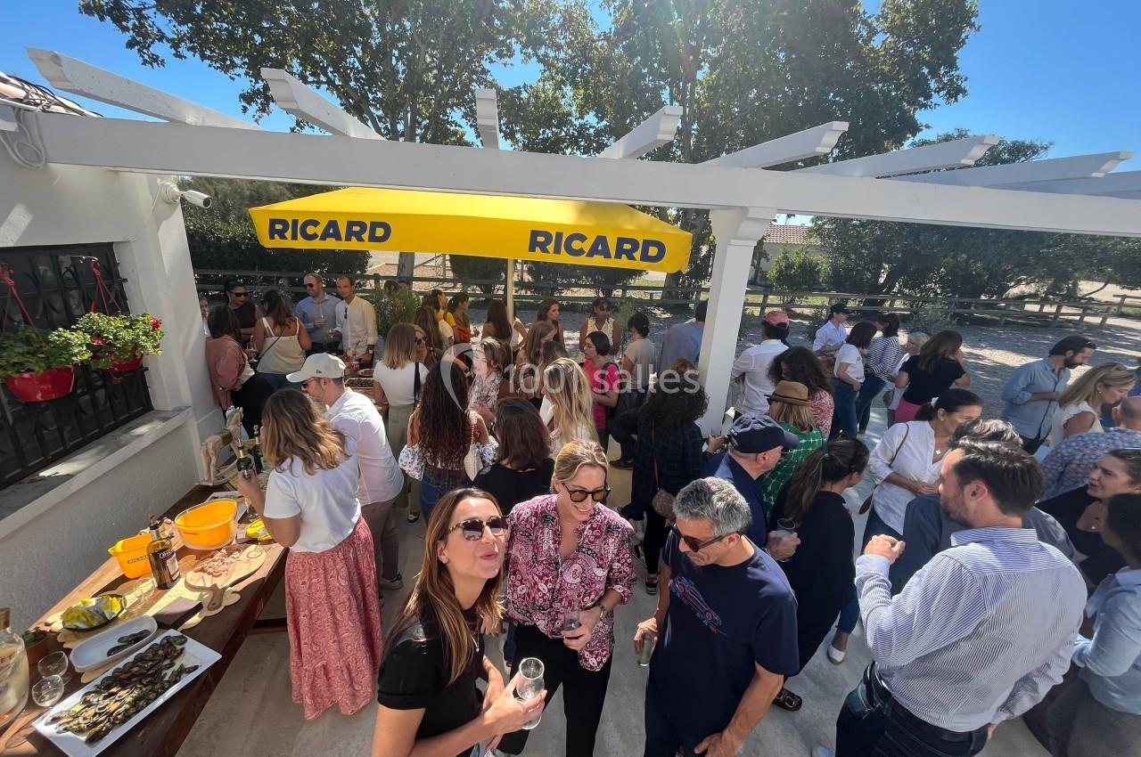 Groupe de personnes rassemblées en extérieur sous un auvent jaune, discutant et partageant un moment convivial.