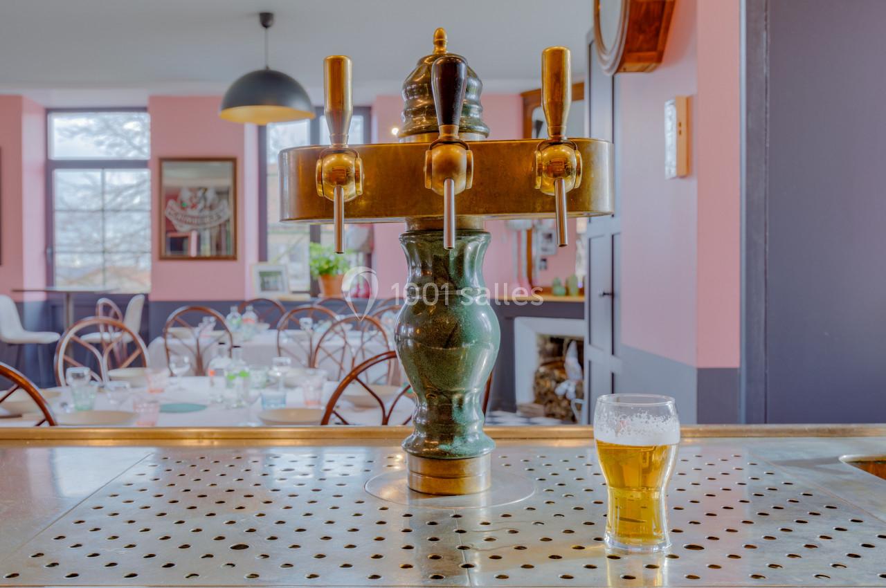 Pompe à bière en laiton sur un comptoir, avec un verre de bière rempli, dans un intérieur de café coloré.