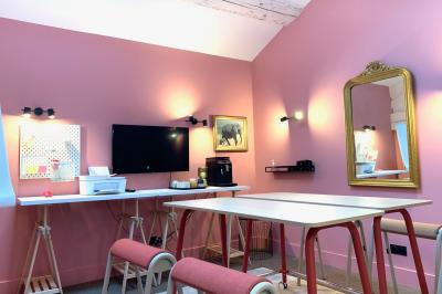 Salle de réunion lumineuse avec murs roses, tables modernes, miroir doré et écran mural.