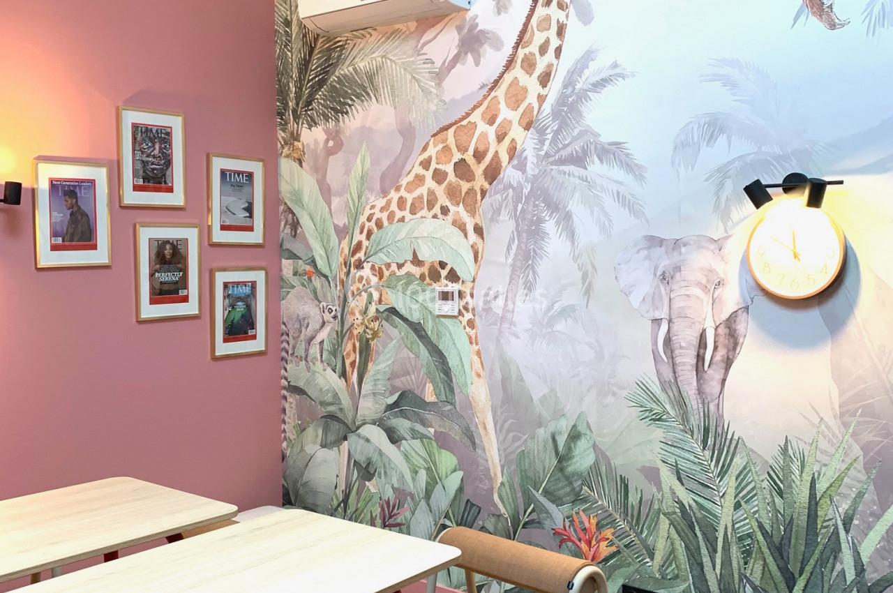 Salle décorée avec des tables, des chaises et une fresque murale représentant des animaux de la savane dans un décor…