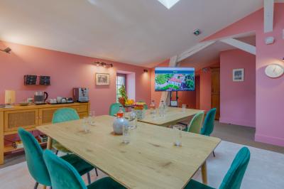 Salle de réunion lumineuse avec murs roses, tables modernes, miroir doré et écran mural.