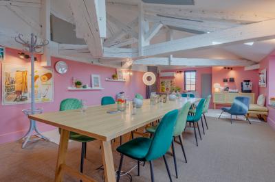 Salle de réunion lumineuse avec murs roses, tables modernes, miroir doré et écran mural.