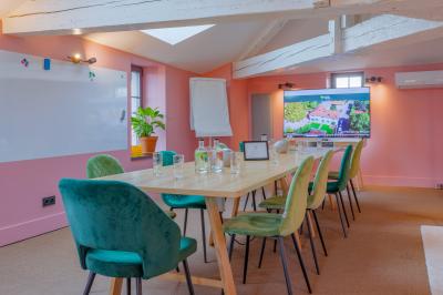 Salle de réunion lumineuse avec murs roses, tables modernes, miroir doré et écran mural.