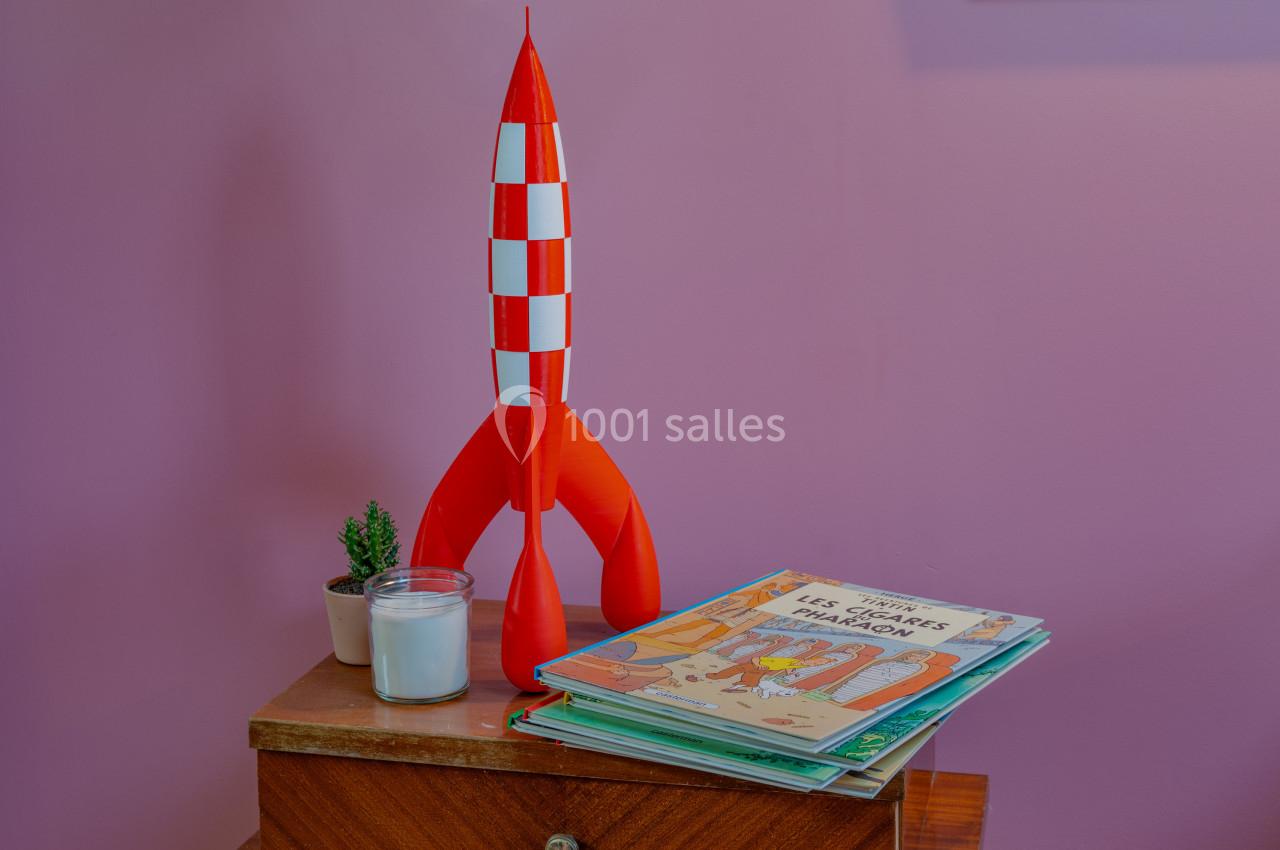 Maquette de fusée rouge et blanche posée sur une table en bois avec une plante, une bougie et des livres pour enfants.