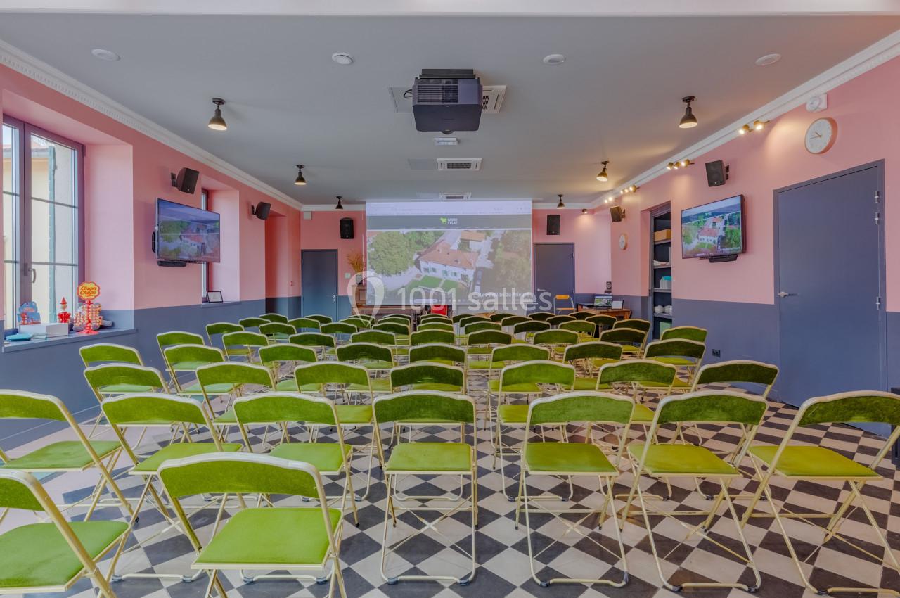 Salle de conférence avec des chaises vertes alignées face à un écran de projection, éclairage intérieur lumineux.