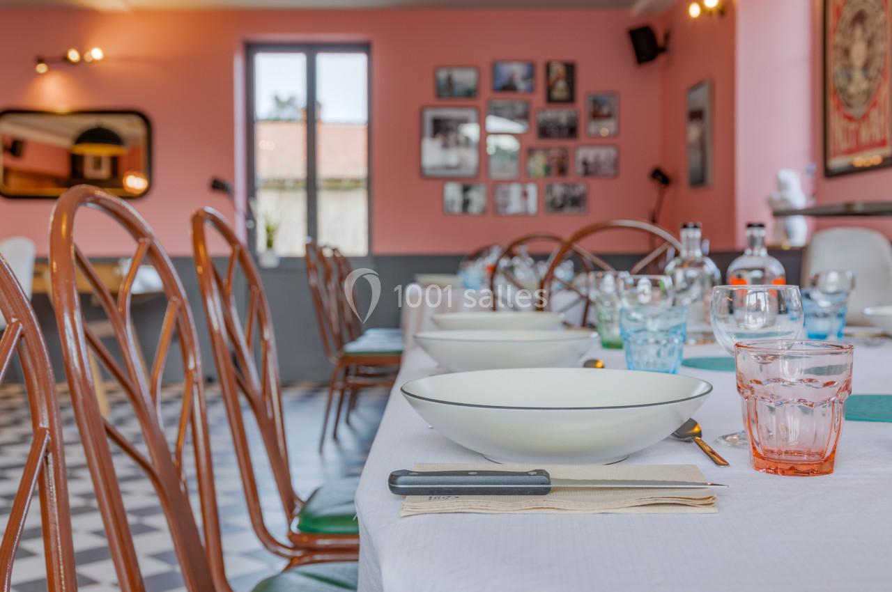Salle de restaurant lumineuse avec tables dressées, chaises en bois, murs roses et décorations murales.
