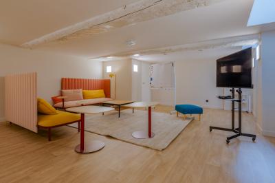 Salle de réunion lumineuse avec murs roses, tables modernes, miroir doré et écran mural.
