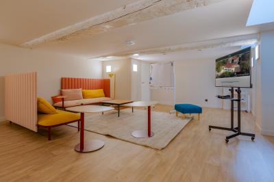 Salle de réunion lumineuse avec murs roses, tables modernes, miroir doré et écran mural.