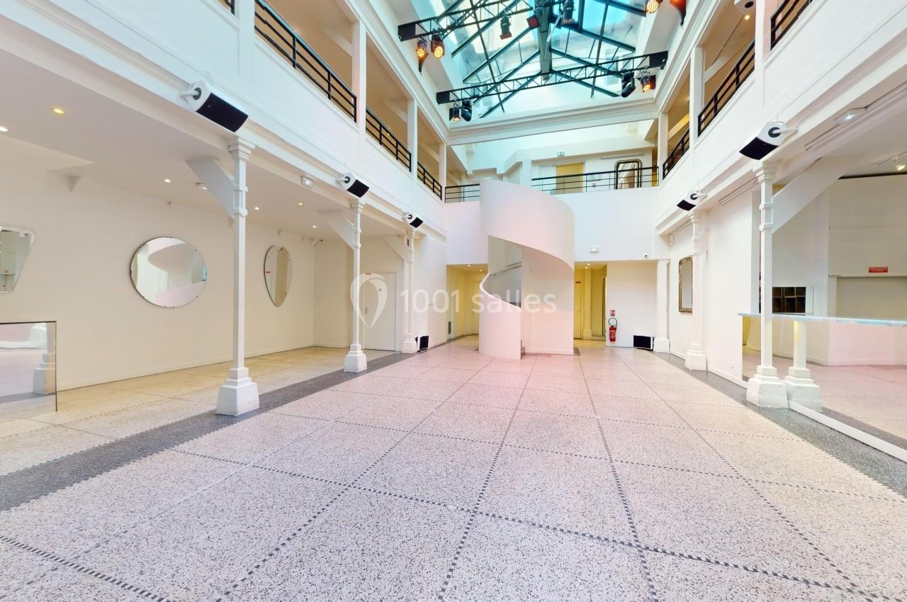 Intérieur d'un espace lumineux avec sol en terrazzo, murs blancs, escalier en colimaçon et verrière au plafond.