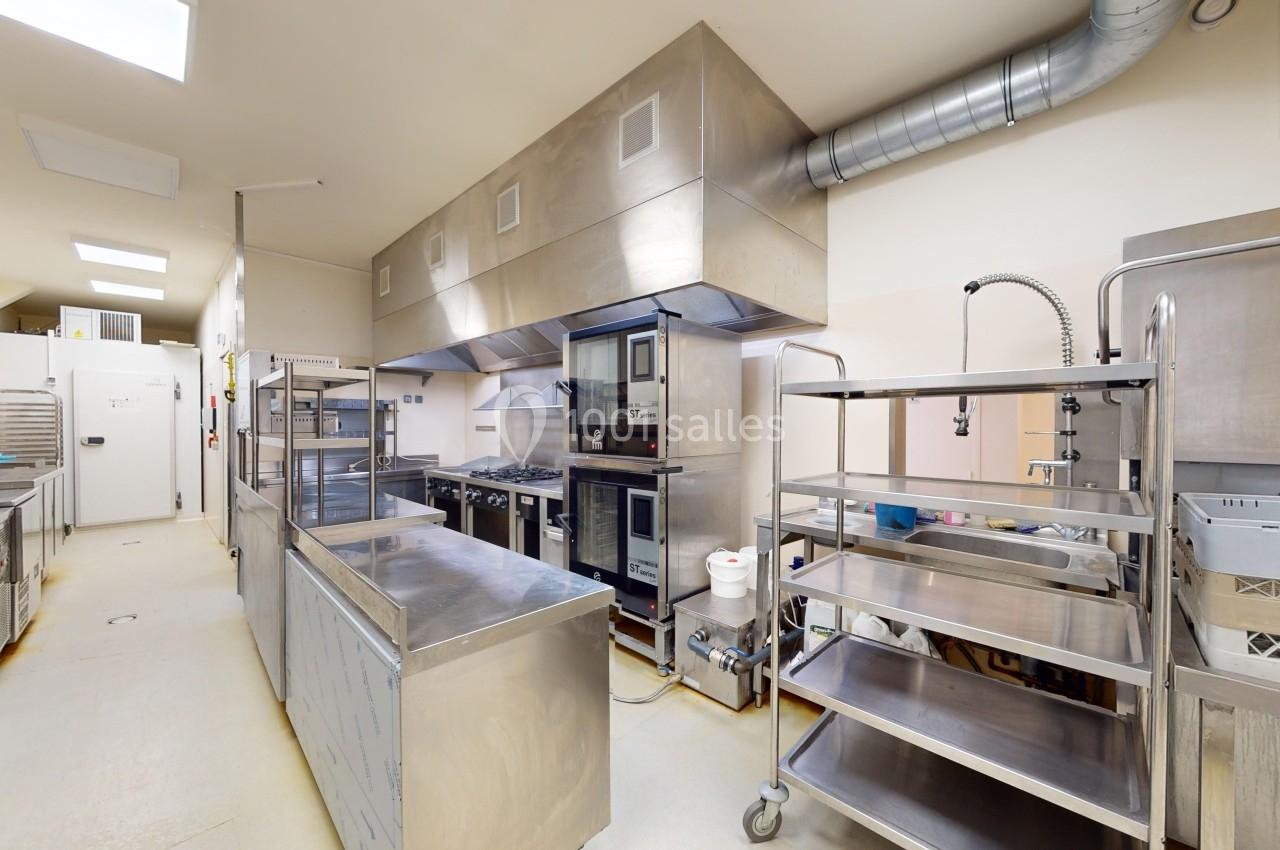 Cuisine professionnelle équipée avec plans de travail en inox, fours, étagères métalliques et système de ventilation.