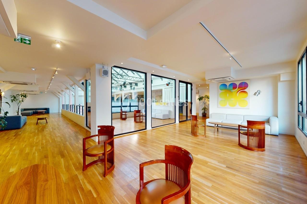 Espace intérieur lumineux avec parquet, mobilier moderne, grandes fenêtres et une cloison vitrée décorée d'une œuvre colorée.