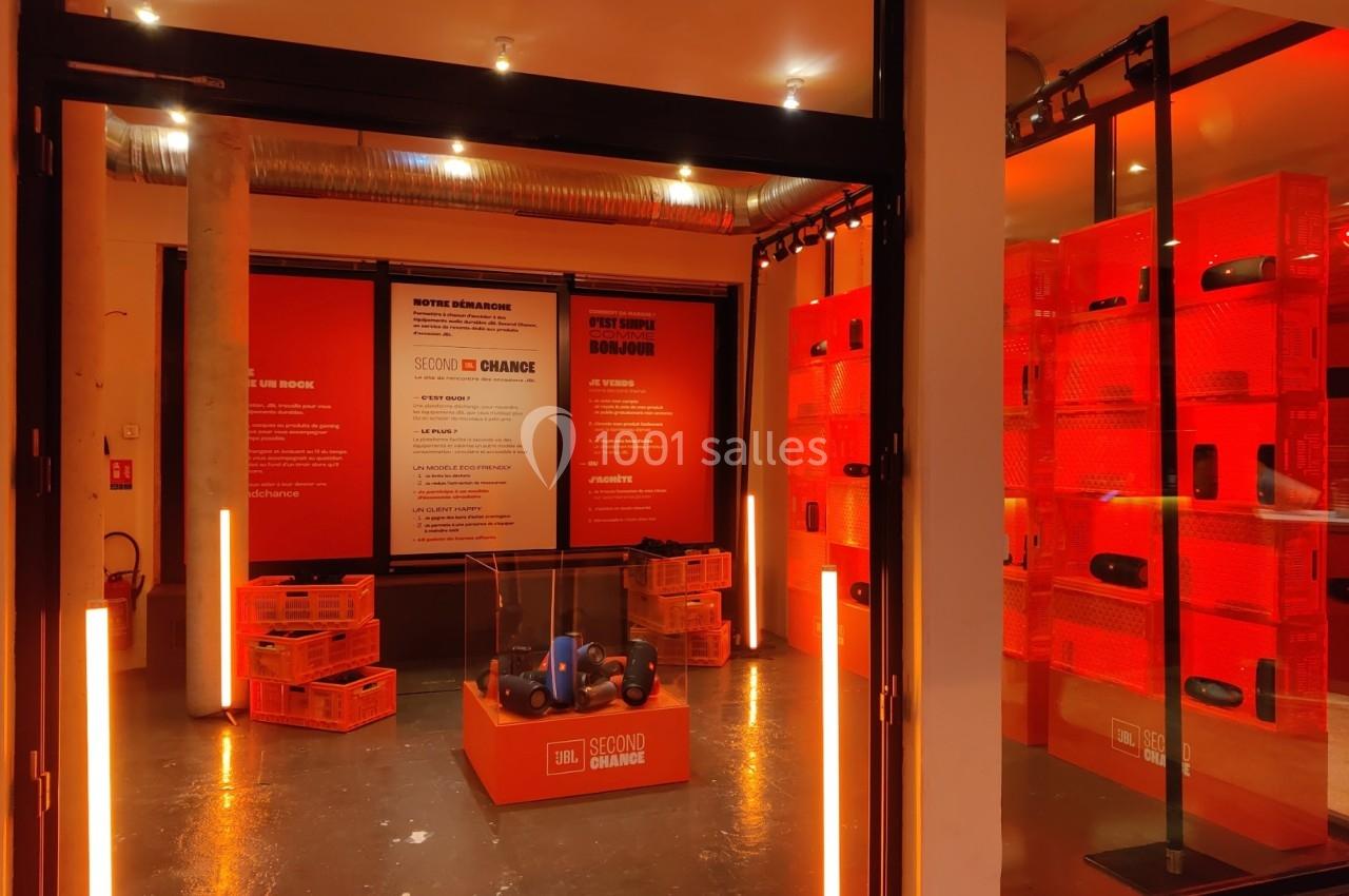 Boutique avec éclairage orange, présentoirs de produits audio et panneaux informatifs sur le recyclage et la seconde main.