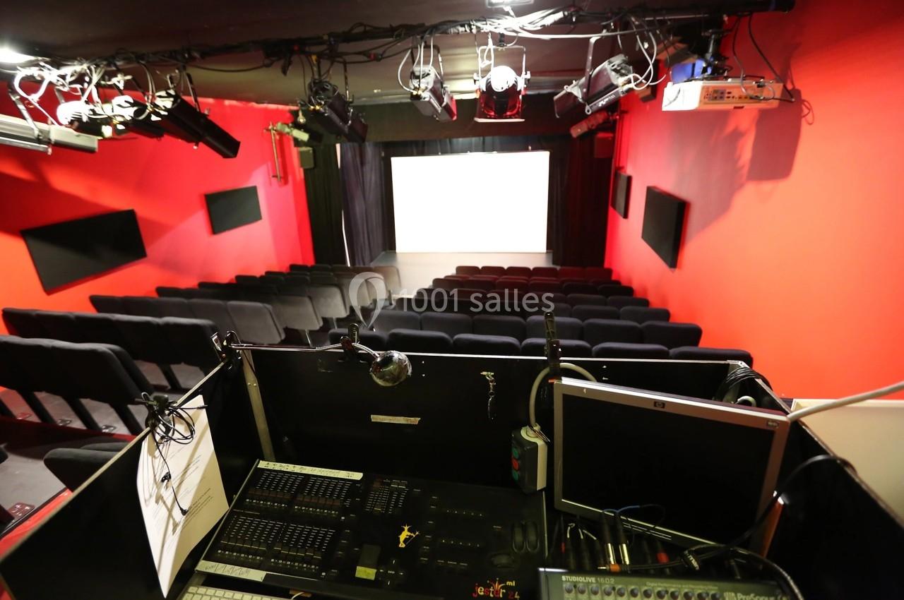 Salle de projection avec rangées de sièges noirs, écran blanc et cabine technique équipée à l'avant-plan.