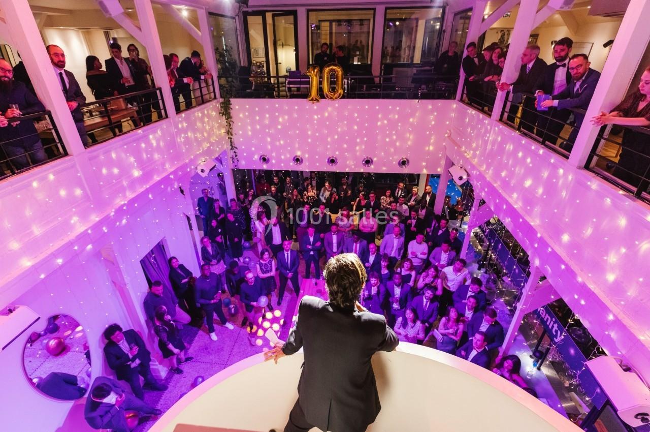 Un orateur s'adresse à une foule lors d'un événement dans un espace décoré de lumières et de ballons dorés.