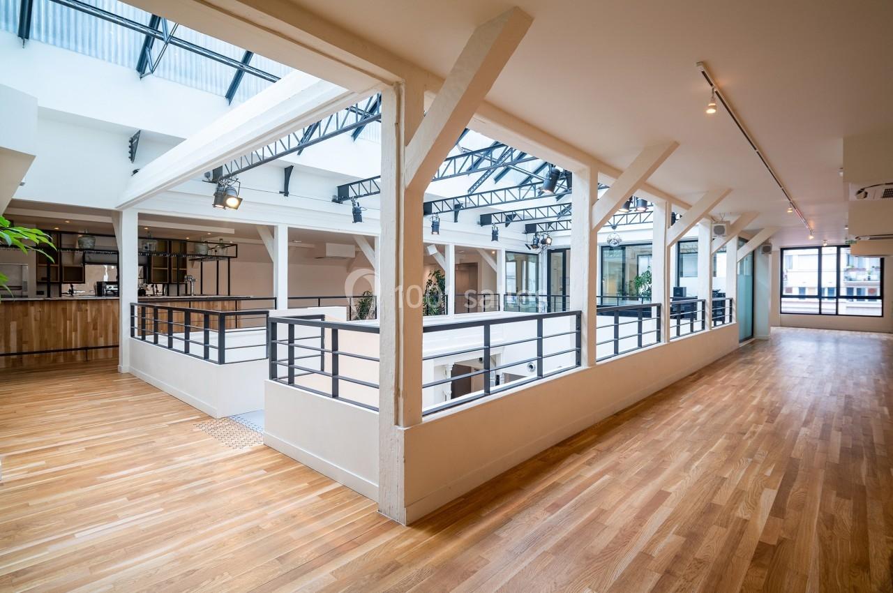 Espace intérieur lumineux avec parquet, verrière et balustrades blanches, donnant sur un étage inférieur.