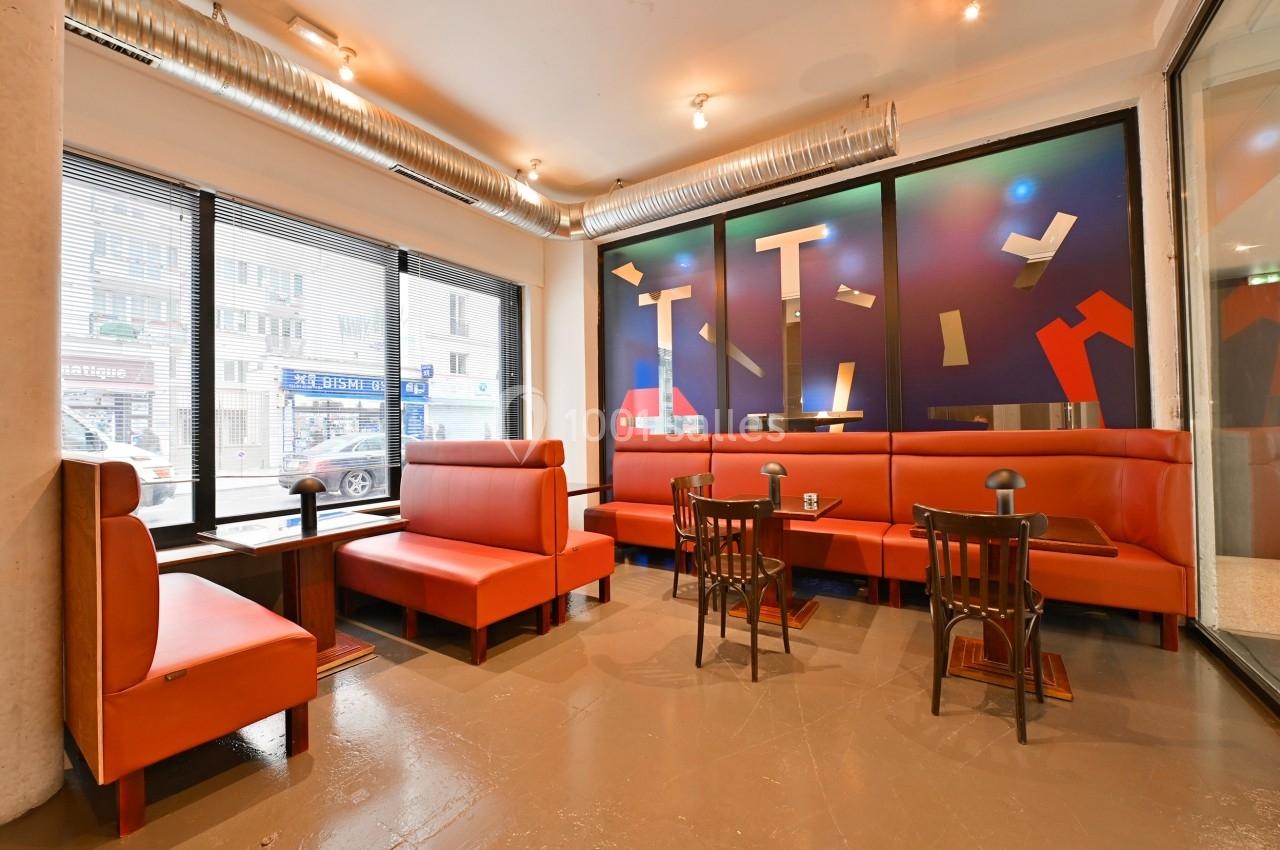 Salle lumineuse avec banquettes rouges, petites tables en bois et grande baie vitrée donnant sur une rue urbaine.