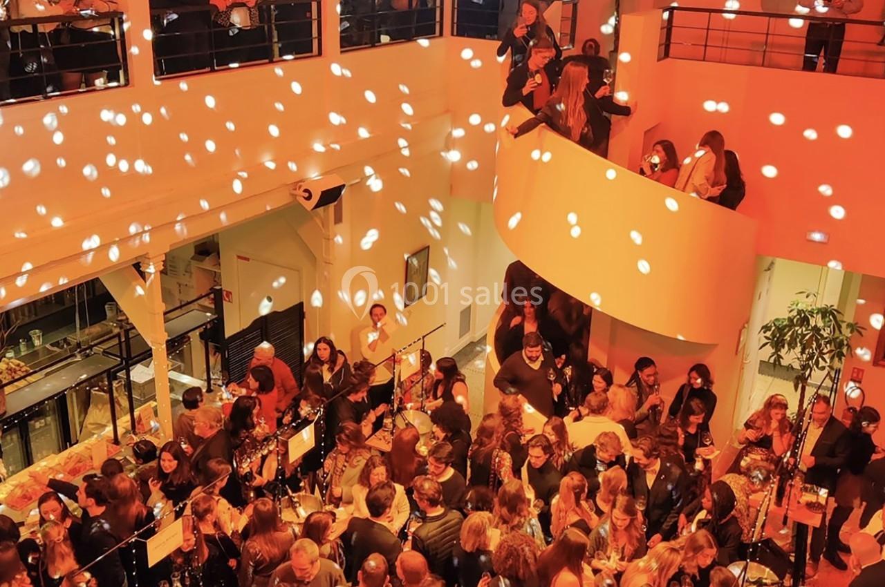 Salle animée avec de nombreuses personnes réunies lors d'un événement, éclairée par des lumières tamisées et des spots.