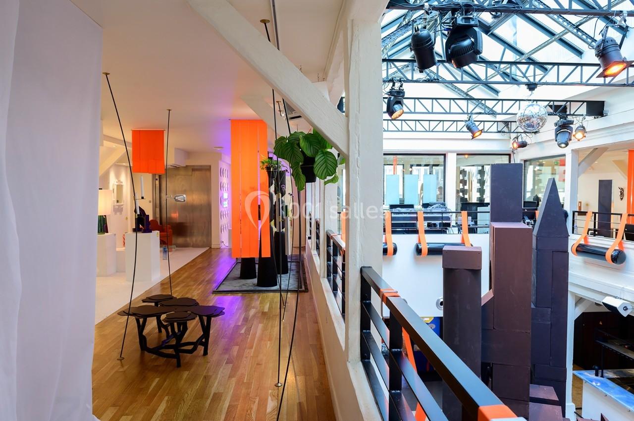 Intérieur lumineux avec mezzanine, verrière, mobilier moderne et éléments décoratifs orange et noirs.