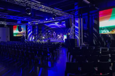 Des personnes discutent et prennent un verre autour de tables en bois devant un bâtiment industriel lors d'un événement.