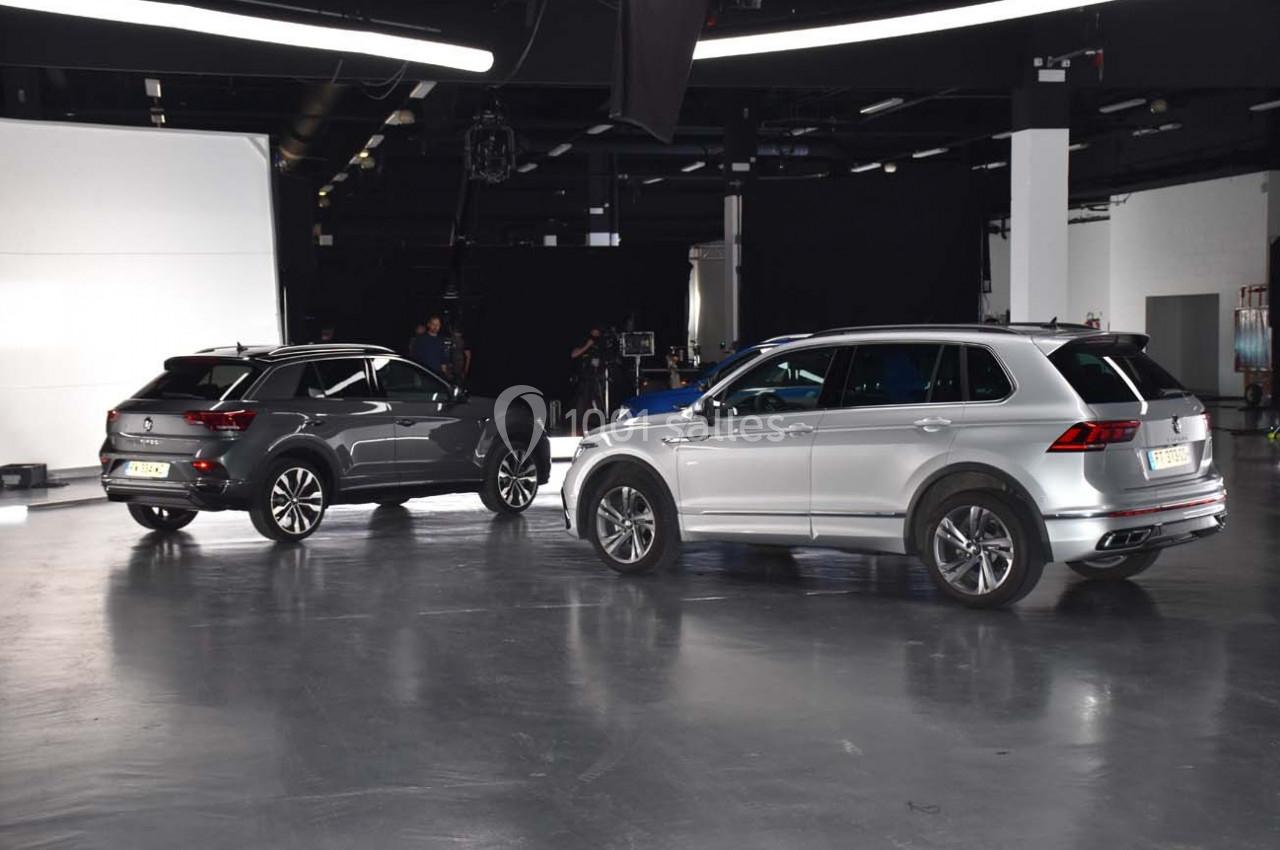 Deux SUV stationnés dans un studio lumineux avec un sol en béton et un fond noir.