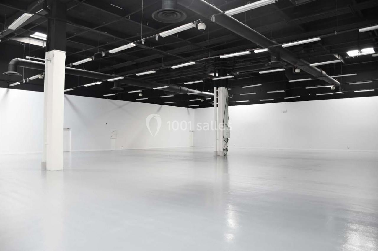 Grand espace intérieur vide avec sol brillant, murs blancs et plafond noir équipé de luminaires industriels.
