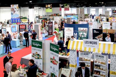 Des personnes discutent et prennent un verre autour de tables en bois devant un bâtiment industriel lors d'un événement.