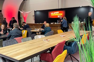 Des personnes discutent et prennent un verre autour de tables en bois devant un bâtiment industriel lors d'un événement.
