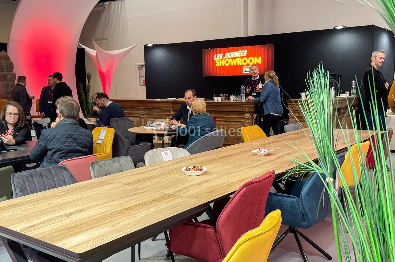 Des personnes discutent et travaillent autour de tables en bois dans un espace showroom avec un éclairage chaleureux.
