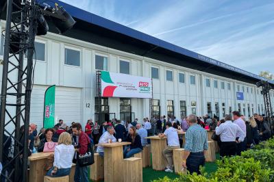 Des personnes discutent et prennent un verre autour de tables en bois devant un bâtiment industriel lors d'un événement.