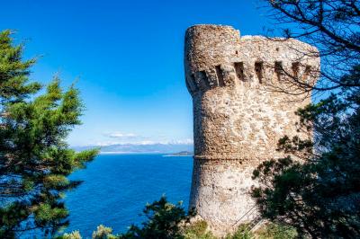 Paysage montagneux au coucher du soleil avec une personne debout sur un promontoire rocheux, entourée de végétation.