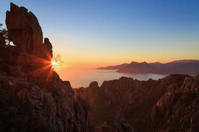 Paysage montagneux au coucher du soleil avec une personne debout sur un promontoire rocheux, entourée de végétation.