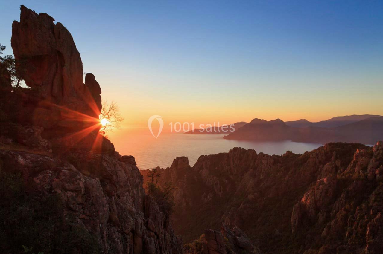 Paysage de montagne au coucher du soleil avec vue sur la mer et un ciel dégradé d'orange et de bleu.