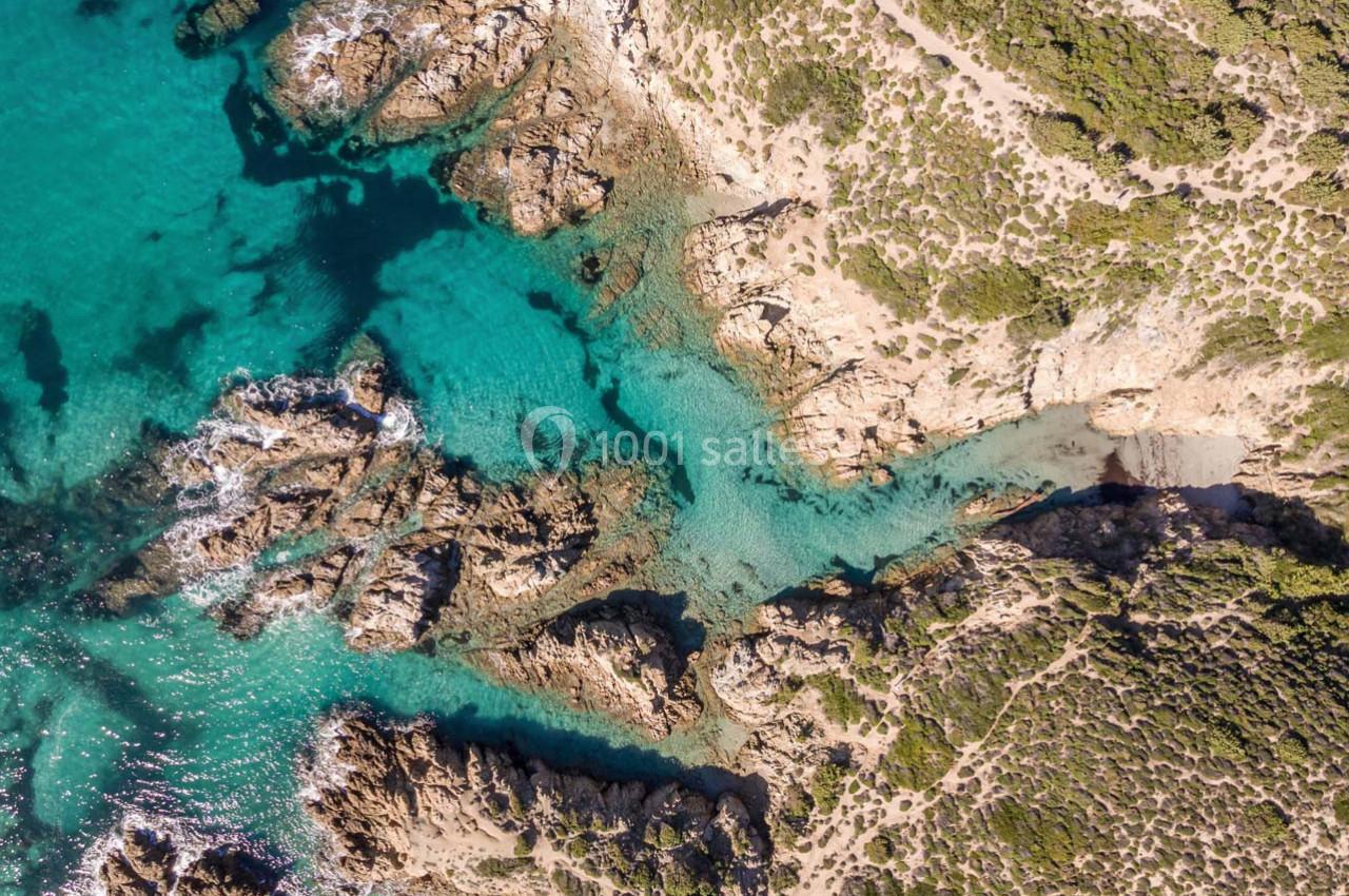 Vue aérienne d'une côte rocheuse avec une eau turquoise et des formations rocheuses entourées de végétation.