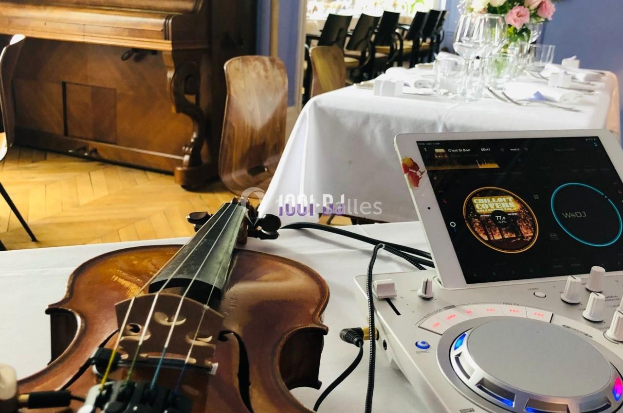 Un violon posé sur une table près d'un contrôleur DJ, dans une salle avec des tables dressées.