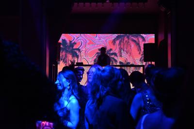 Personnes dansant et discutant dans une ambiance tamisée de boîte de nuit avec un écran lumineux en arrière-plan.