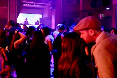 Personnes dansant et discutant dans une ambiance tamisée de boîte de nuit avec un écran lumineux en arrière-plan.