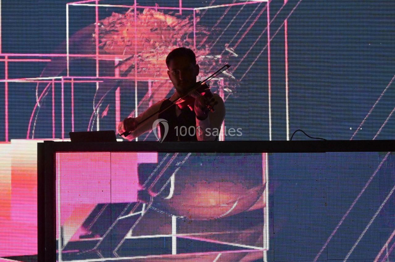 Un musicien joue du violon sur une scène éclairée par des projections lumineuses abstraites roses et noires.