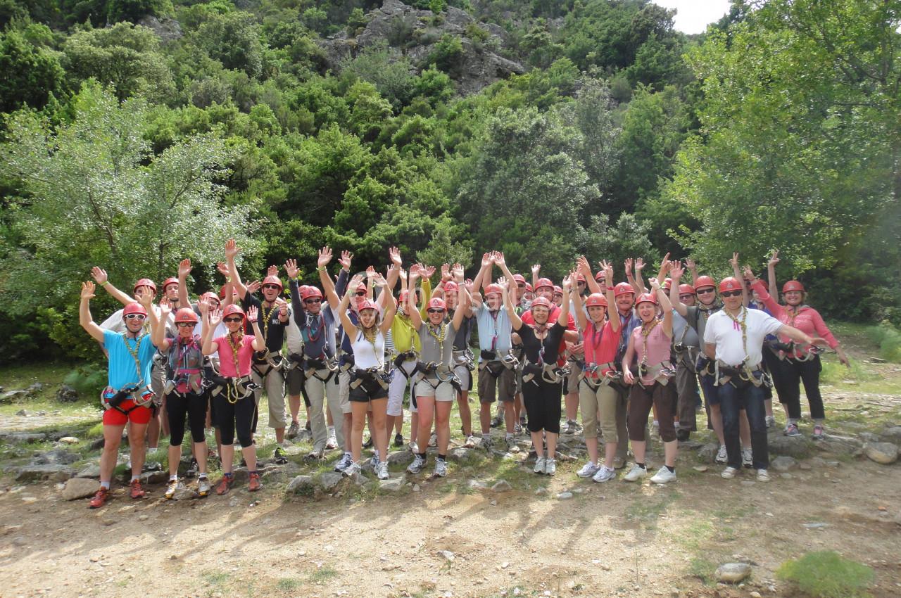 Un groupe de personnes en tenue d'escalade lève les bras devant un paysage boisé.