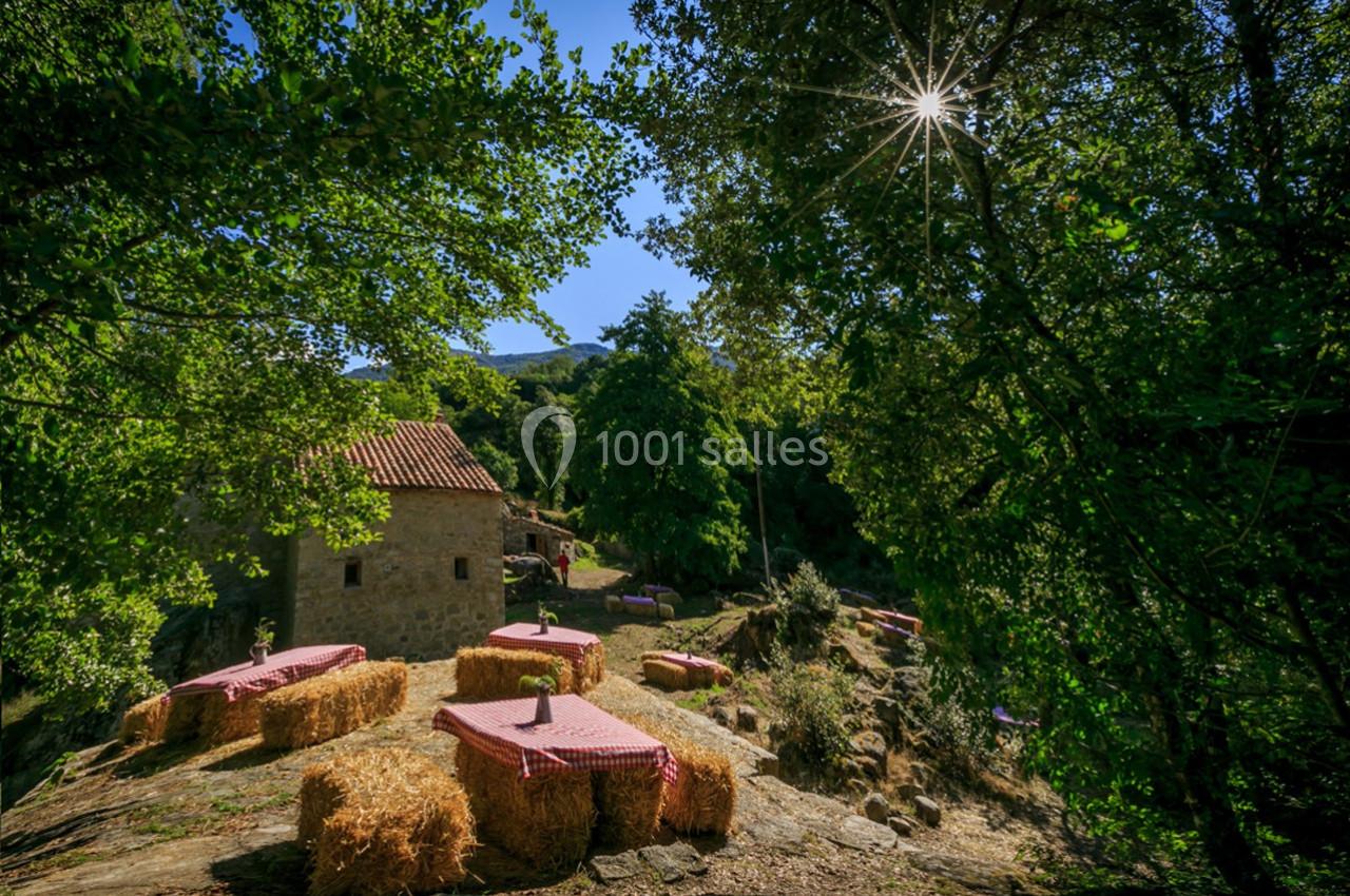 Tables en plein air avec nappes rouges posées sur des bottes de foin, entourées de verdure et éclairées par le soleil.