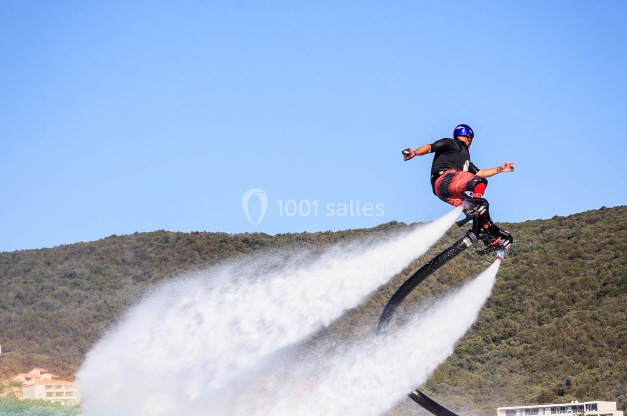 Un homme équipé d'un flyboard s'élève au-dessus de l'eau avec un paysage de collines en arrière-plan.