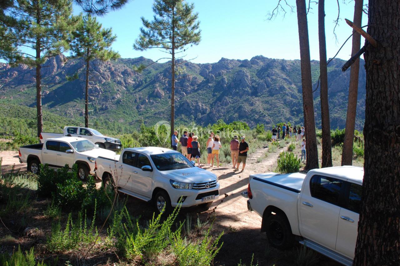 Des véhicules tout-terrain blancs stationnés près d'un sentier de randonnée en montagne, avec des personnes marchant au loin.