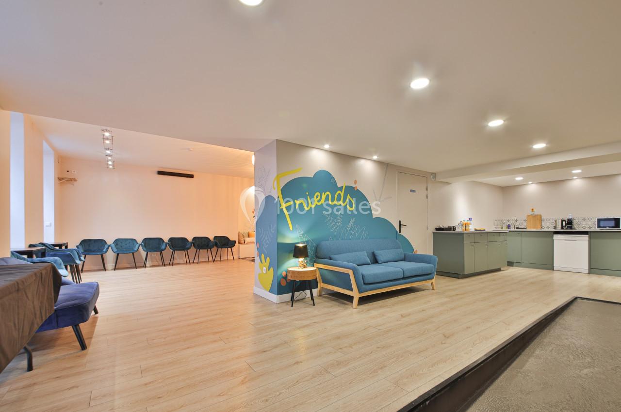 Salle lumineuse avec coin salon, kitchenette équipée et rangée de chaises alignées contre un mur clair.