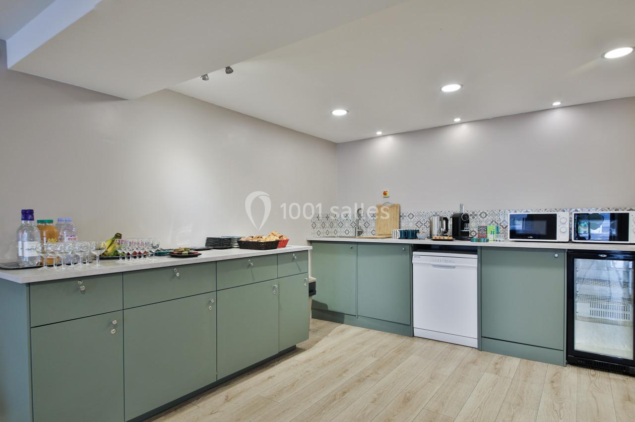 Cuisine moderne avec des placards verts, un plan de travail équipé d'appareils électroménagers et un sol en bois clair.