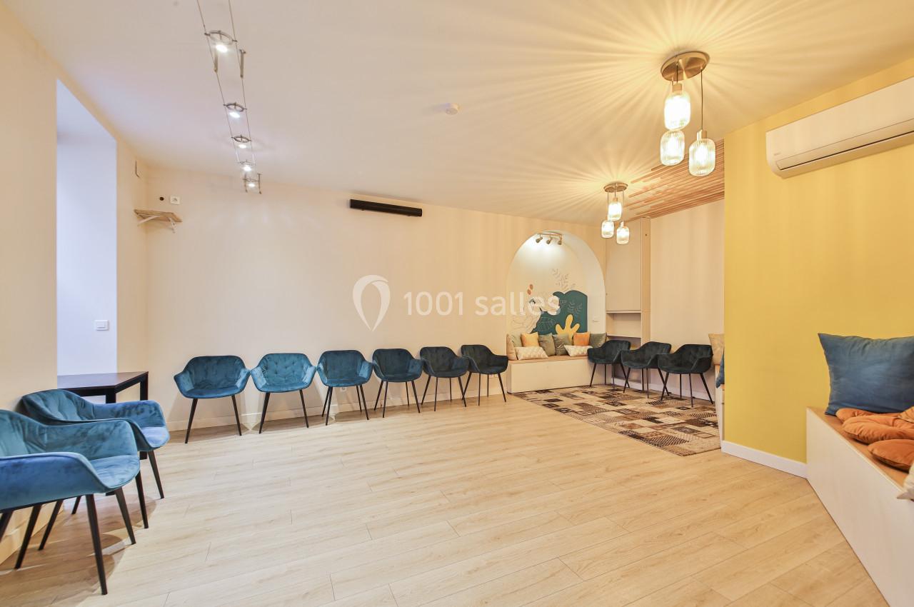 Salle lumineuse avec des chaises bleues disposées en cercle, parquet clair et mur décoré d'une fresque colorée.